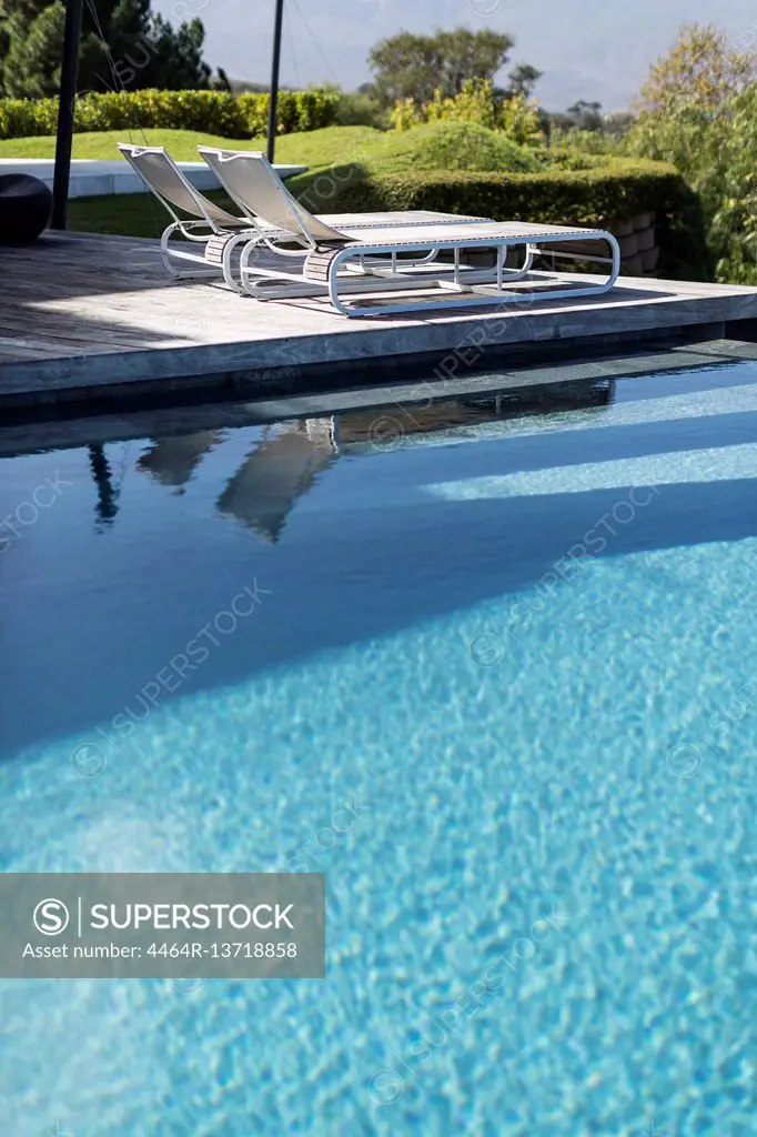Sunny, tranquil blue swimming pool and lounge chairs