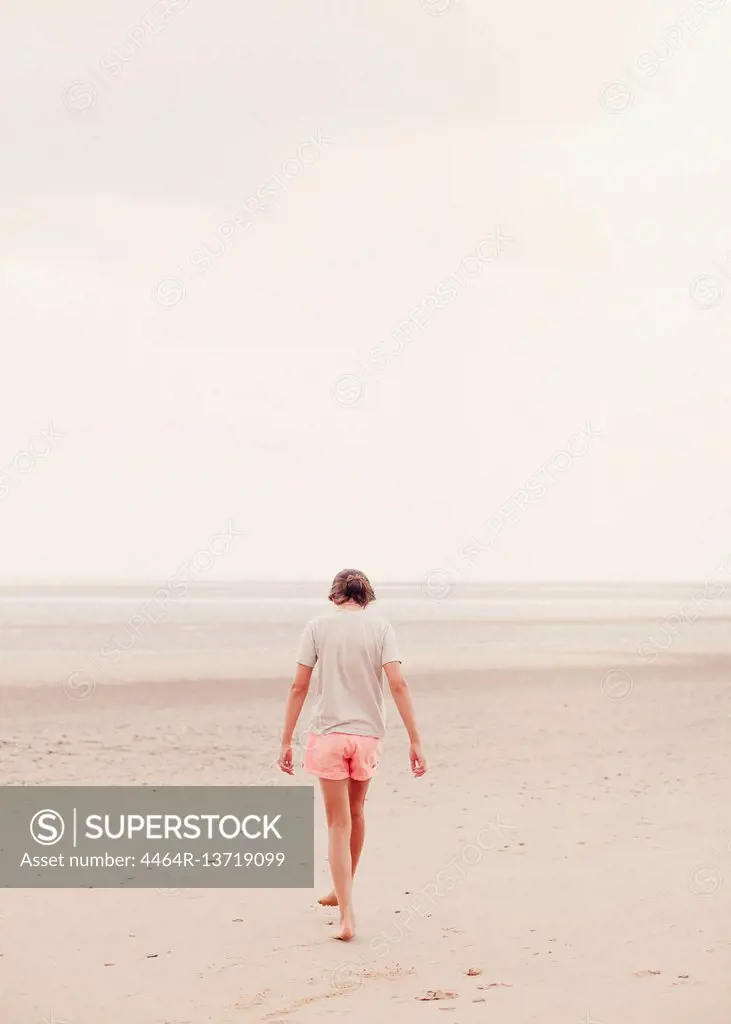 Teenage girl walking in sand on overcast summer beach