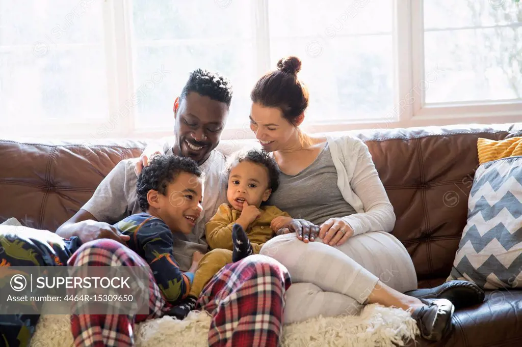 Multi-ethnic young family relaxing in pajamas on living room sofa