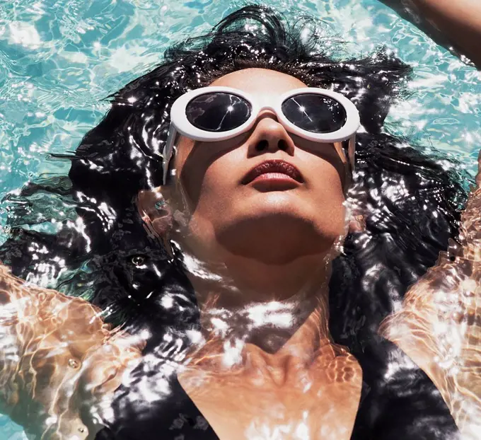 Close up serene woman in sunglasses relaxing, floating in sunny summer swimming pool