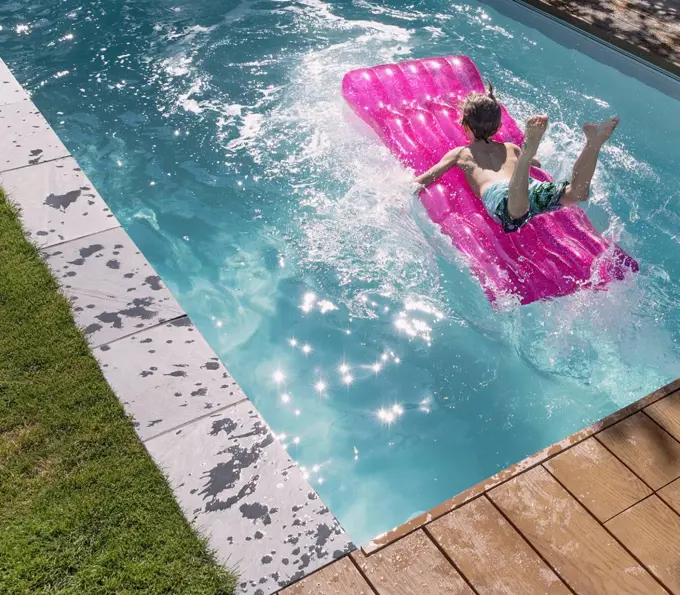 Playful boy jumping on inflatable raft in sunny summer swimming pool