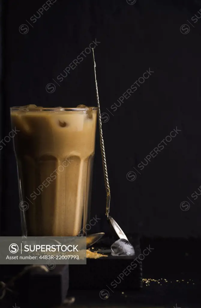 Iced coffee with milk in a tall glass, black background, selective focus