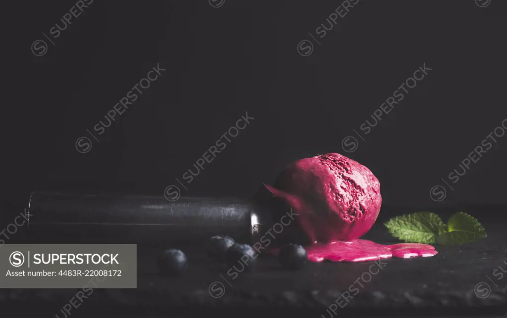 Melting blueberry ice-cream scoop over black slate stone background, selective focus, copy space, horizontal composition