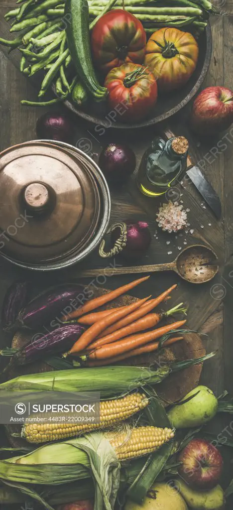 Fall cooking background. Autumn ingredients for Thanksgiving day dinner preparation. Flat-lay of green beans, corn cobs, carrot, tomatoes, eggplant, pears, apples over wooden table, top view