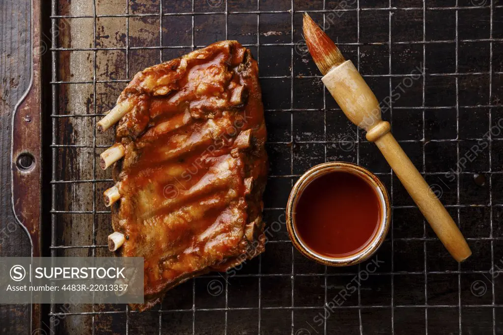 BBQ grilled smoked pork ribs and sauce brush on dark metal baking sheet background
