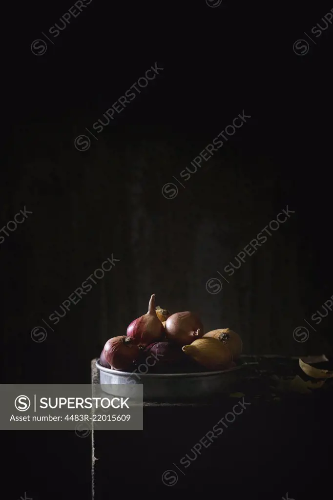 Yellow and purple onions in vintage aluminum plate over black table in the dark. Dark rustic style. With copy space at top.