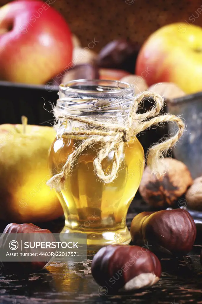 Glass jar of honey with apples, chestnuts and walnuts over black wooden table