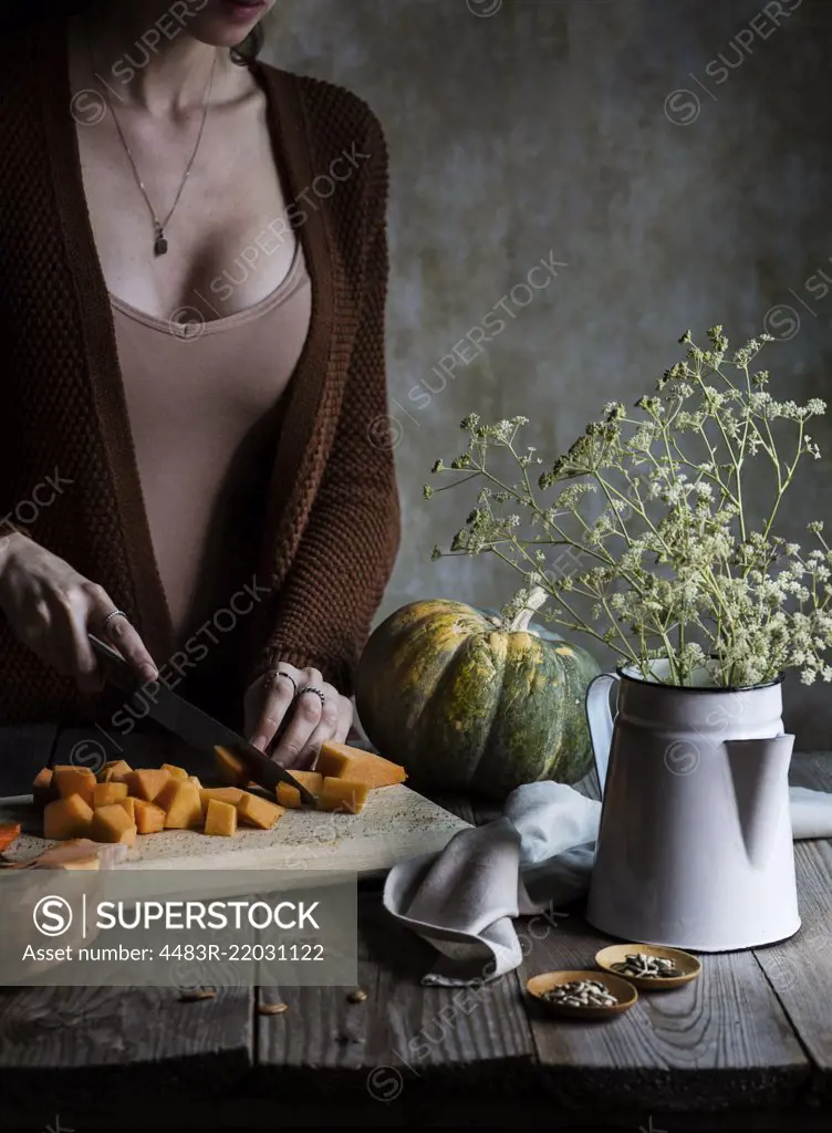 Woman cutting fresh pumpkin on a rustic wooden table