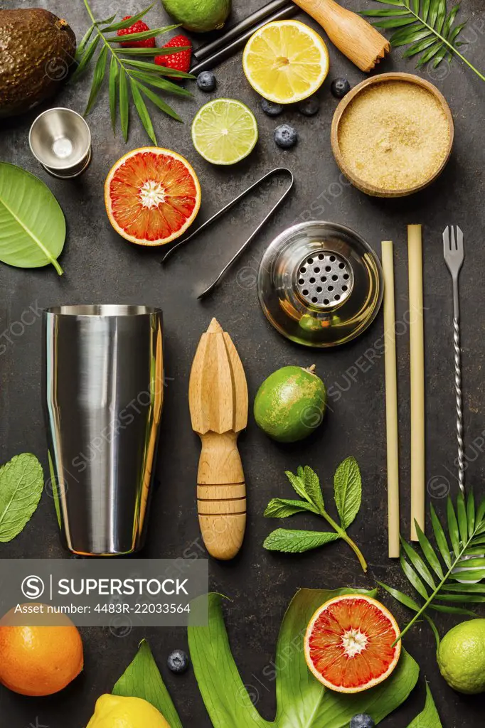 Cocktail making bar tools, shaker, tropical fruits and leaves on a dark background. Top view