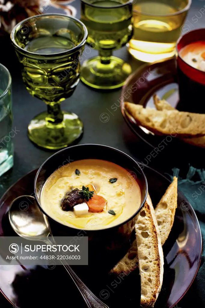 Wine Roasted Vegetable Bisque served with bread and wine. Photographed on a dark blue background.