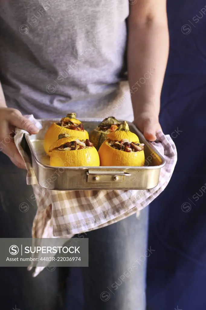 Female hands holding a pan with roasted stuffed zucchini
