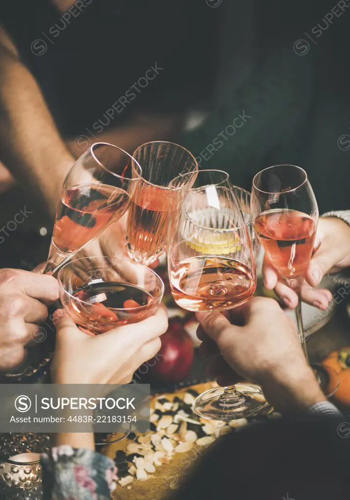 Traditional Christmas or New Year holiday celebration party. Friends or family feasting and clinking glasses with rose wine at festive Christmas table with homemade snacks