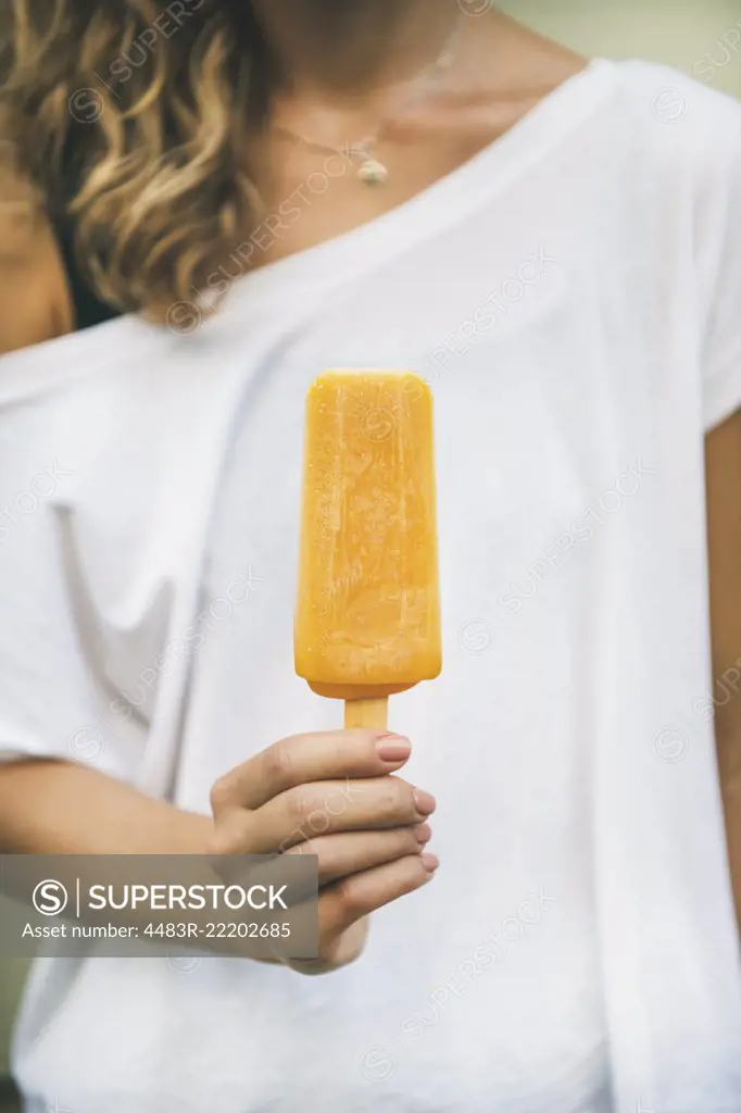 Healthy vegan orange mango citrus ice cream popsicle in hand of young woman. Summer dessert and cheerful summer mood concept