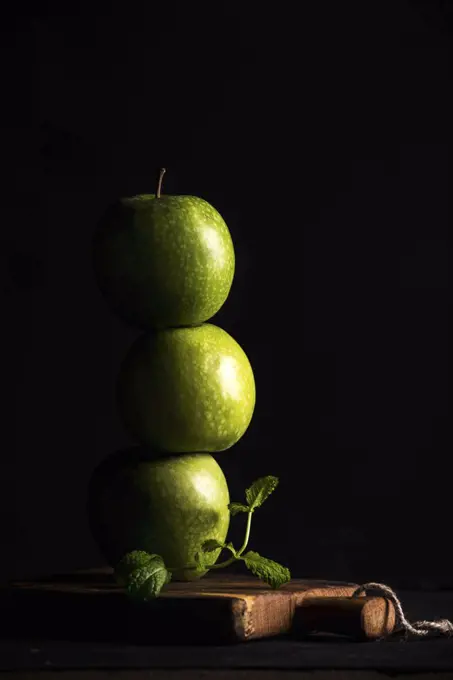 Green apples making stack or tower with branch of fresh mint on black background, copy space
