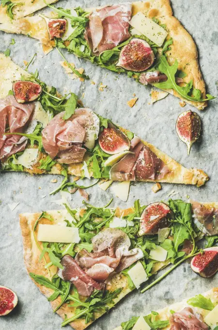 Pieces of fig, prosciutto, arugula and sage flatbread pizza on baking paper, top view, vertical composition