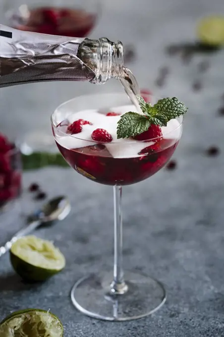 A glass of Raspberry and Pomegranate Champagne Cocktail is being topped of with champagne