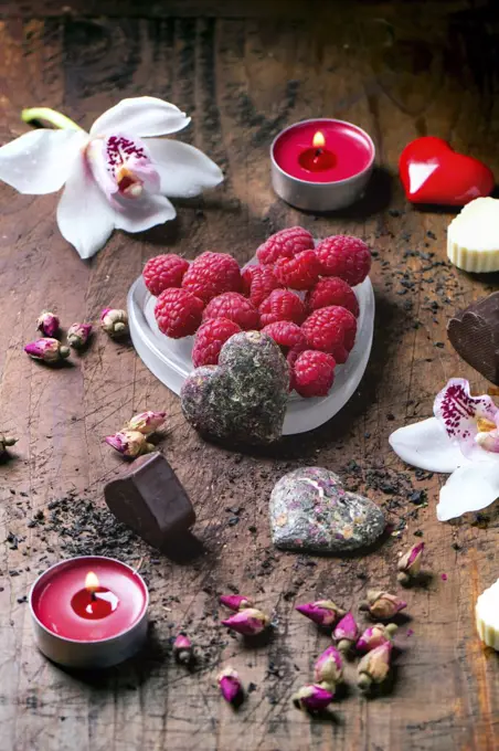 Chocolate candies heart shaped with dry tea roses, fresh raspberries and orchids for Valentine's Day.