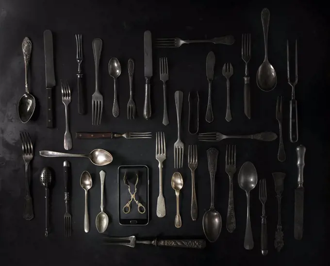 Big set of vintage cutlery with smartphote over black metal background. Top view