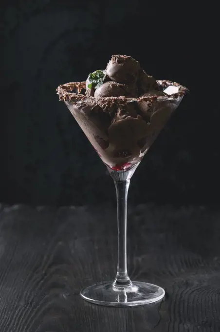 Cocktail glass with chocolate ice cream mini balls with fresh raspberries and mint on black burnt wooden background. Dark toned image