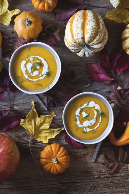 Pumpkin and sweet potatoes soup in bowls topped with cream and fresh dill, Autumn leaves on a rustic wooden table