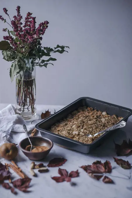Pear and cinnamon baked oatmeal in a baking pan and coconut sugar in a bowl on white marble table