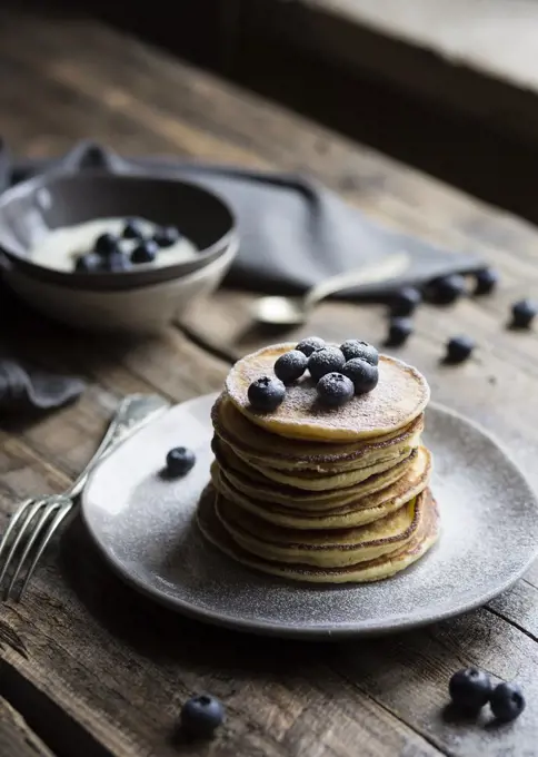 Breakfast table with pancakes served with blueberries and icing sugar and yogurt