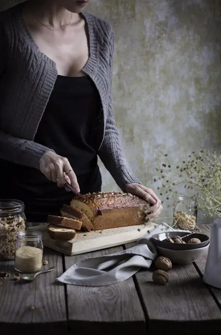 Woman cutting muesli cake on a rustic wooden table