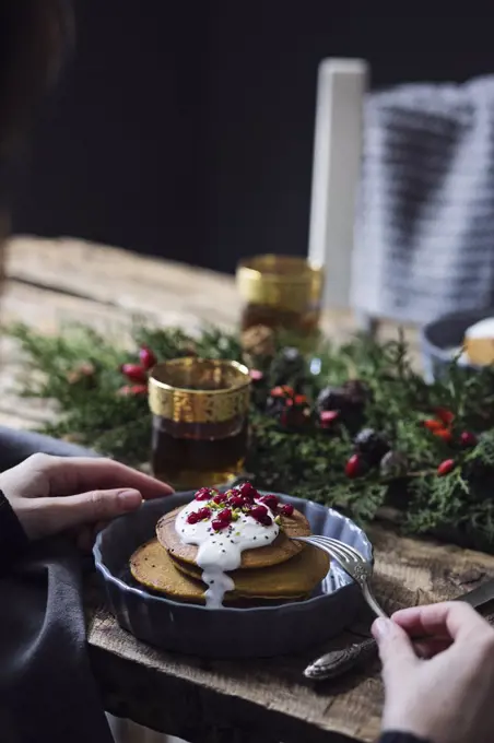 Christmas breakfast table: Woman eating pumpkin pancakes with yogurt cream and currant