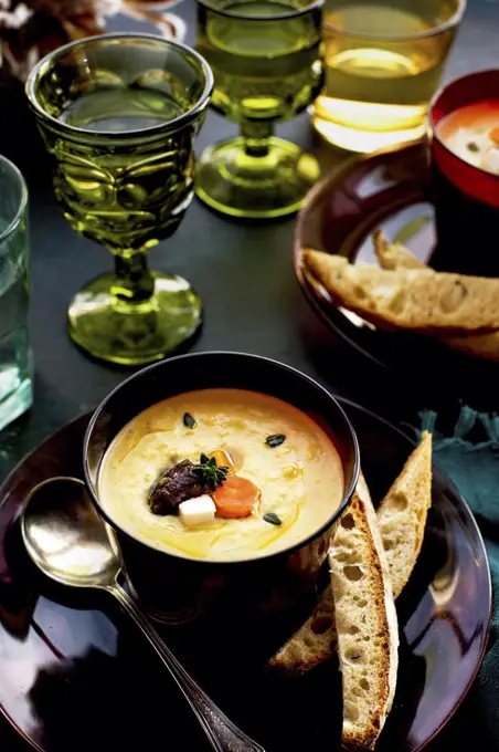 Wine Roasted Vegetable Bisque served with bread and wine. Photographed on a dark blue background.