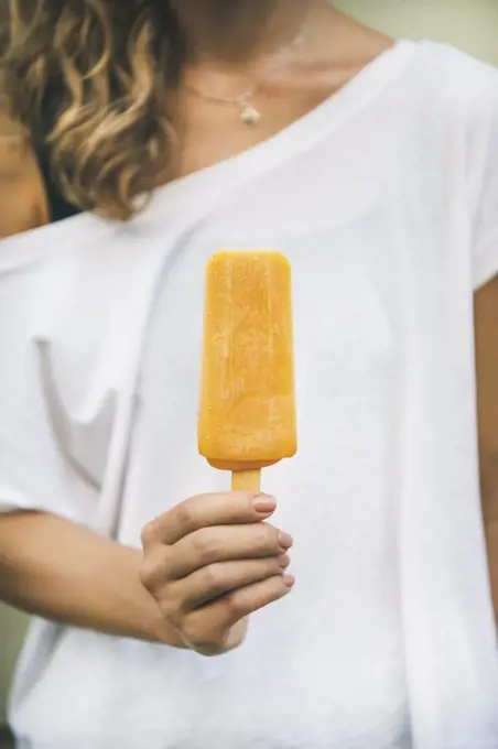 Healthy vegan orange mango citrus ice cream popsicle in hand of young woman. Summer dessert and cheerful summer mood concept