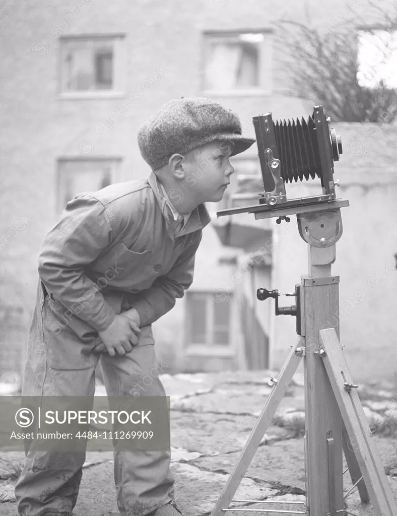 Boy in the 1940s. A curious child is looking into a camera mounted on a tripod.   Sweden 1945. Kristoffersson Ref N107-5