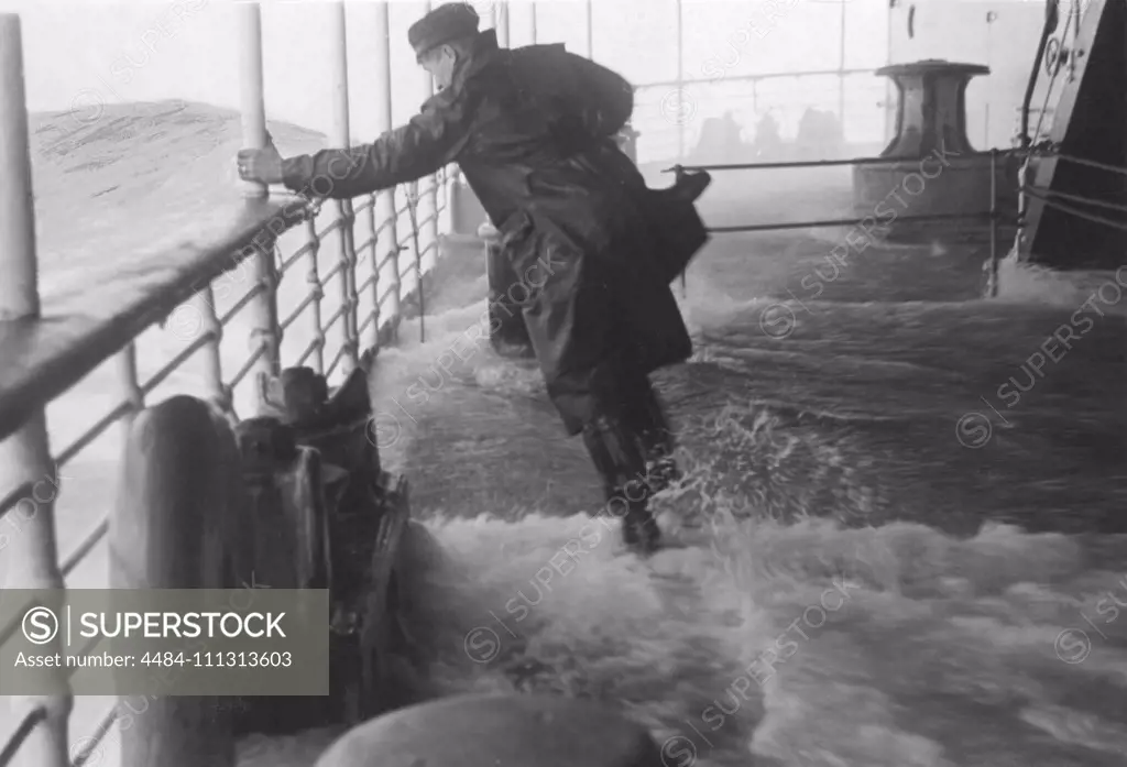 Rough weather at sea. A sailor is struggling to stand up straight on the ships deck as water and wind makes the ship turn and twist. Sweden 1940s