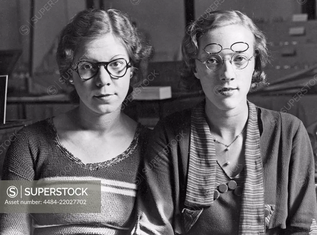 1930s glasses. Two women each wearing a pair of glasses presented as the new shape of glasses and bows. To the left 1935 years shape of glasses and bow. To the right a pair of glasses with which combines two sets of lenses. One set for reading and the other for ordinary wear, easily folded up and down depending on situation. England 1935