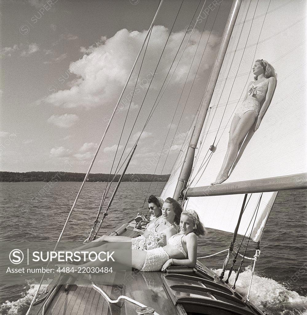 1940s sailing boat. Four young women are aboard the sailing boat and  enjoying the sunshine on deck. One of the girls is leaning against the  sail. They are wearing the typical 1940s bathingsuit and bikini with high  waist. Sweden 1946 Photo Kristoffersson
