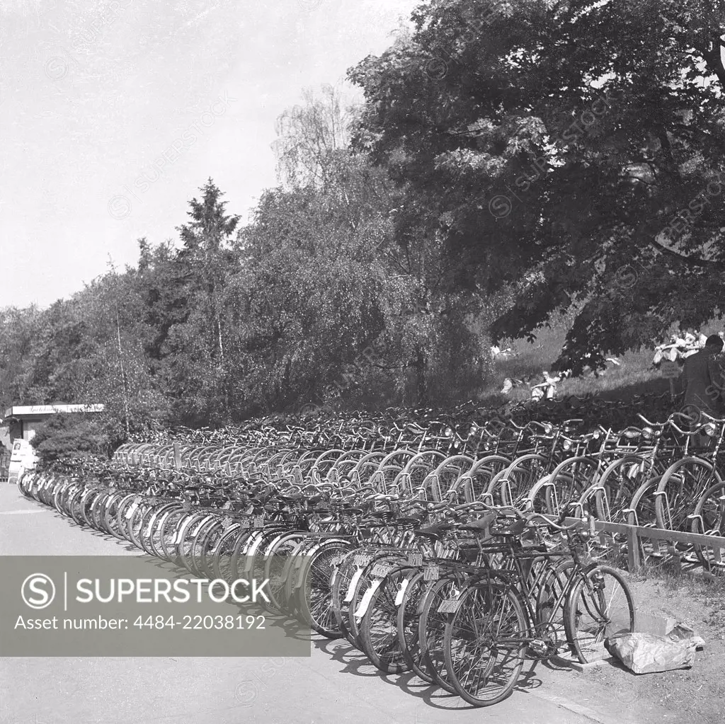 1940s cyclists. Bicycles are parked at a public bath a warm summer day. The bicycles are properly parked in cycle racks. Note the registration signs on the bikes that was a mandatory item at the time. May 1940. Photo Kristoffersson 129-11