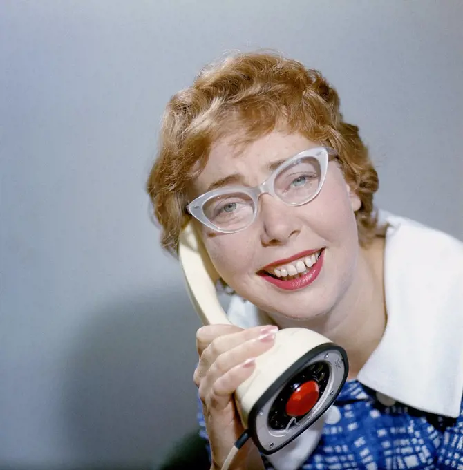 1950s glasses and telephone. A young woman in typical fifties glasses and bows is talking on the telephone. Swedish on-piece plastic telephone created by Ericsson Company of Sweden and launched 1956. Because of its styling and its influence on future telephone design, the Ericofon is considered one of the most significant industrial designs of the 20th century. The idea was to incorporate the dial and handset into one single unit. To call, you lifted it up and dialed the number, and to end the 