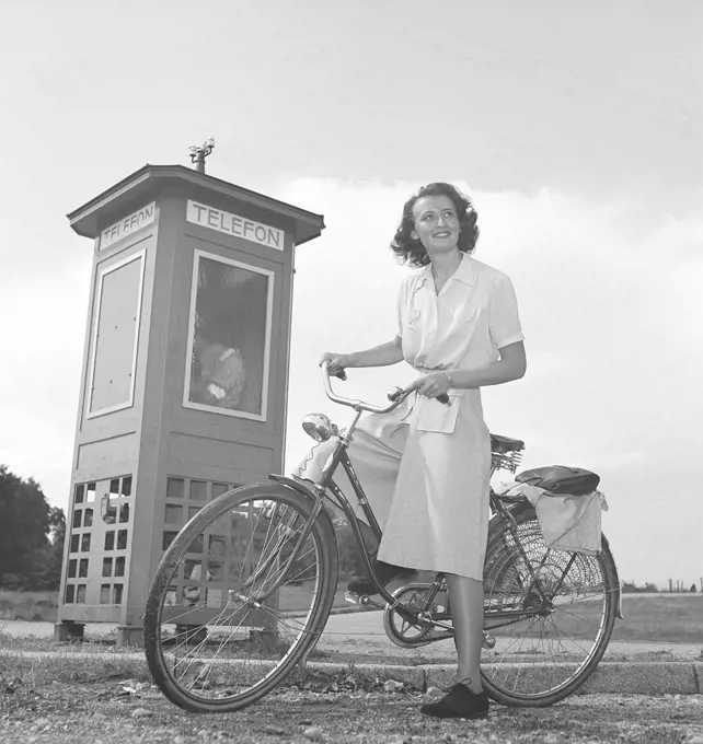1940s woman on a bicycle. A smiling young woman on a womens bicycle beside a phone booth. Notice the protection detail on the back wheel to protect ladies clothing from being caught in the wheel. Sweden 1940s. Photo Kristoffersson M47-1