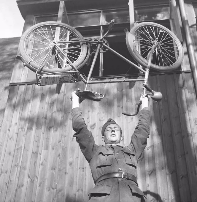 1940s soldier. A young man in uniform is balancing his bicycle above his head. Photo Kristoffersson E90-1