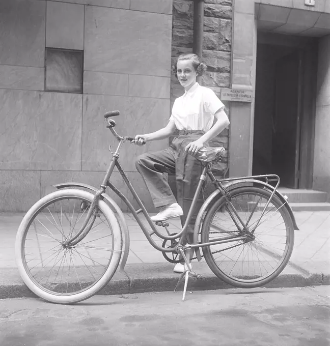 1950s woman on a bicycle. A smiling young woman on a womens bicycle. She has trousers and a white shirt. Sweden 1950s. Photo Kristoffersson BD90-8