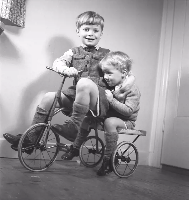 1940s children. Two boys are playing on a tricycle. The older brother is pedaling and the younger brother is sitting on the back. Sweden 1944. Photo Kristoffersson ref M122-6