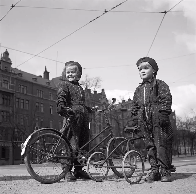 1940s children. Two children are outside with their bicycles. The older girl has a two wheel childrens bicycle, and her younger brother a tricycle. Sweden 1942. Photo Kristoffersson ref A89-5