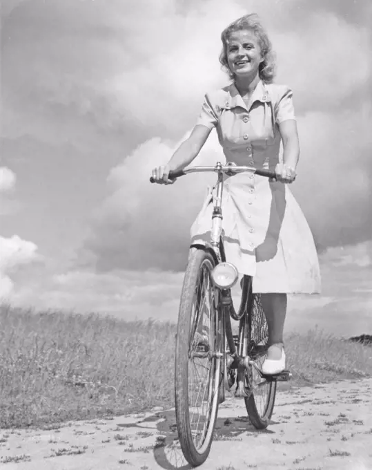 1940s woman on a bicycle. A smiling young woman on a womens bicycle on a sunny day. Sweden 1946
