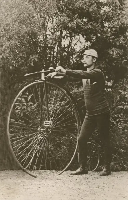Penny farthing bicycle. A man is standing beside a penny-farthing bicycle. A bicycycle model with a large front wheel and a small back wheel. Sweden 1880s