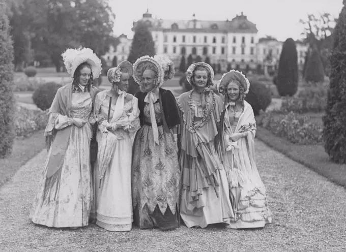 Poke bonnets. A group of five young women in the park of Drottning holm castle, during the filming of the movie Filmen om Emelie Högqvist 1939. They are all dressed up as ladies of the year 1835. Especially the hats whitch are called Poke bonnet that came into fashion at the beginning of the 19th century.