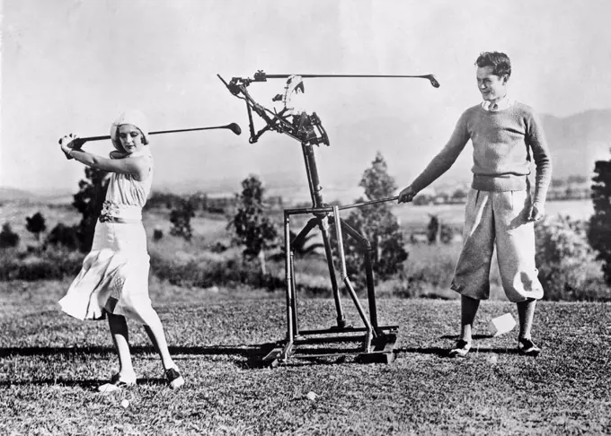Woman learning to play golf in the 1930s. A young woman gets help from a robot golf instructor to perfect her swing. 