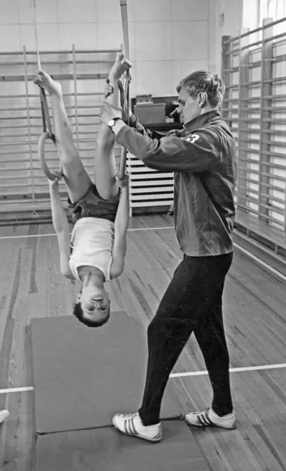 School gymnastics in the 1970s. A teacher is helping a young boy balancing during gymnastics class. Sweden 1970s