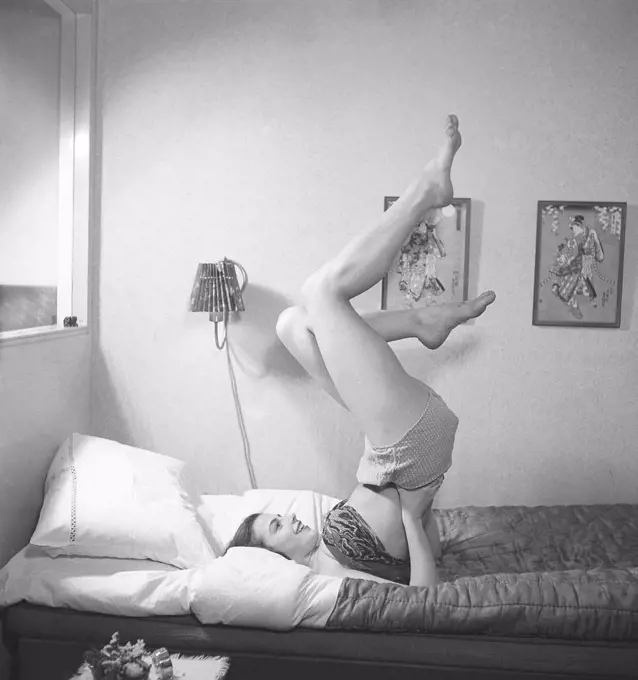 Morning exercise in the 1940s. A young woman is lying in bed and holding her legs up while moving around to get the in shape for the day. Sweden 1940s. Photo Kristoffersson ref Y22-1