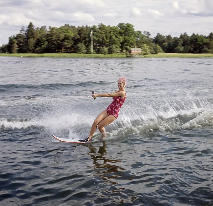 Waterskiing in the 1960s. A young woman in a patterned bathing suit passes the photographer on her waterskis. She has a typical bathing cap on. Sweden 1946 Photo Kristoffersson ref CV12-7