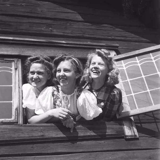 Girls at midsummer. Three young swedish girls in traditional costumes is hanging out of a window at an air midsummer fiest. Sweden Photo Kristoffersson Ref 219-9. Sweden 1940s