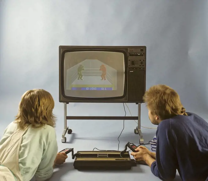 Home video games in the 1980s. A home video game console from Intellivison released by Mattel electronics in 1979. Pictured two people playing a boxing game on a television set.